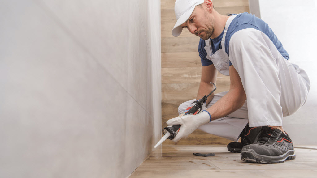 Tradesperson applying sealant along a wall-floor joint during a bathroom fit-out