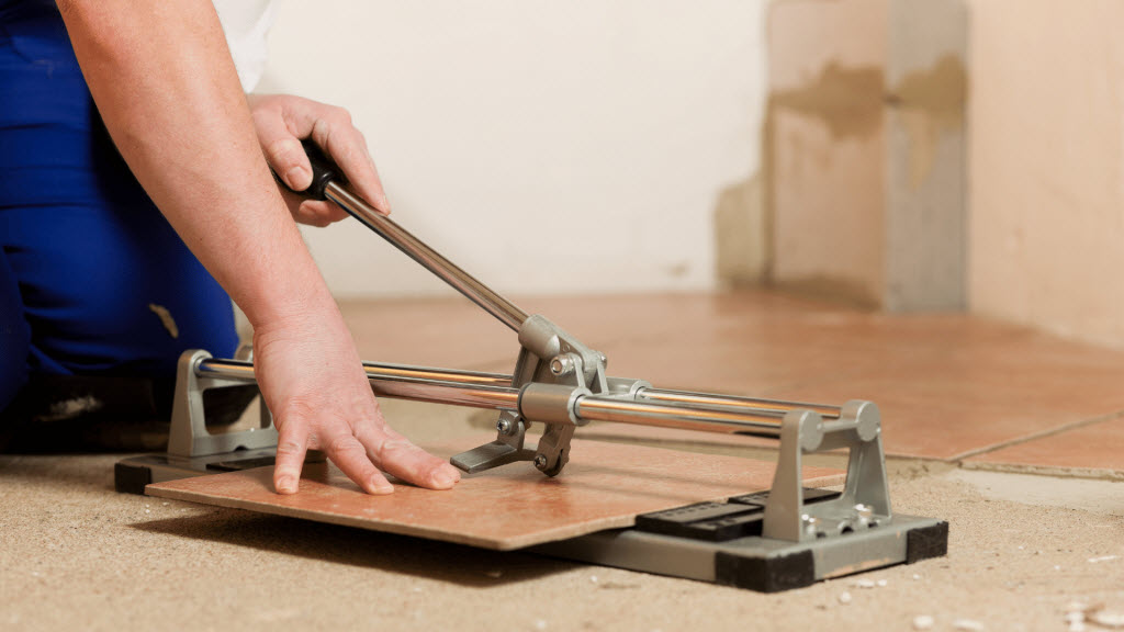 Tradesperson using a manual tile cutter to score a floor tile on a renovation site