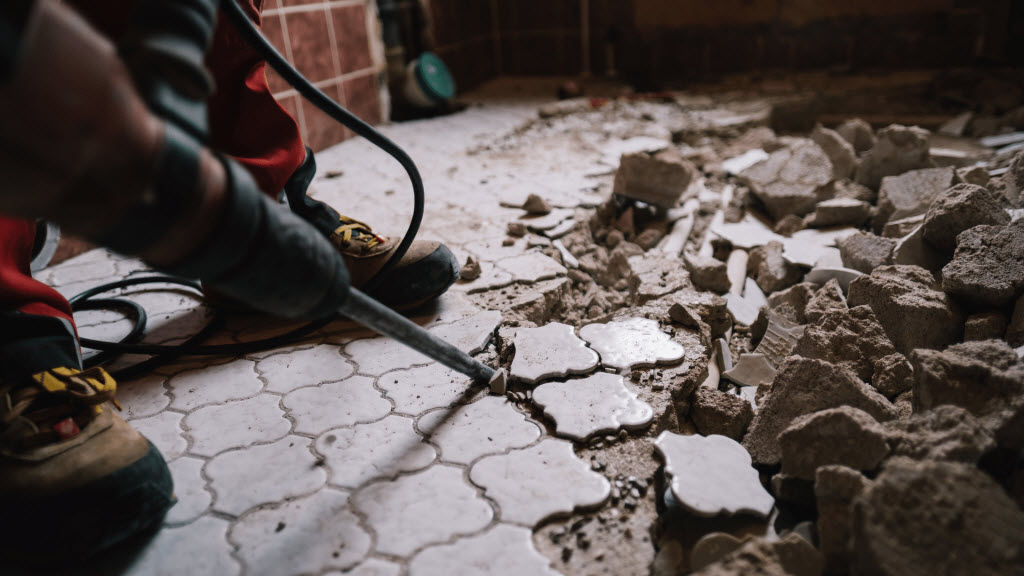 Tradesperson using a demolition hammer to break up old floor tiles during a renovation