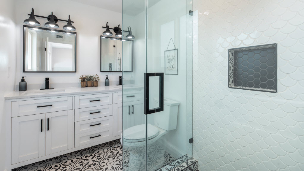 Bathroom with a glass shower screen, scalloped white wall tiles, and a black-framed mirror