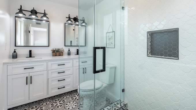 Bathroom with a glass shower screen, scalloped white wall tiles, and a black-framed mirror